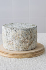 Whole round blue cheese wheel on wooden cutting board on light background, selective focus