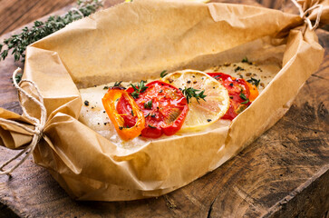 Traditional baked cod fish fillet with vegetable and herbs in backing paper served as close-up on a...