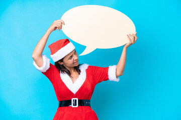 Young hispanic woman dressed as mama noel isolated on blue background holding an empty speech bubble and with sad expression