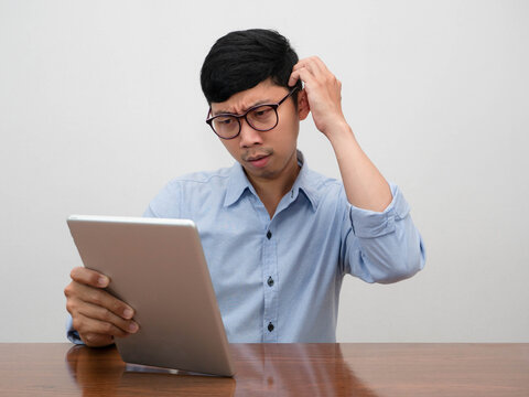 Asian businessman serious looking at tablet in hand gesture sratch head thoughtful about work sit at table