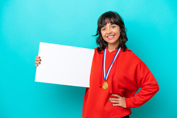 Young latin woman with medals isolated on blue background holding an empty placard with happy expression