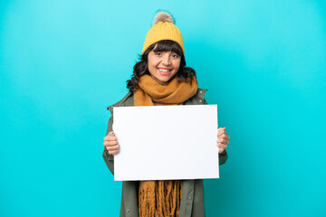 Young latin woman wearing winter jacket isolated on blue background holding an empty placard with happy expression