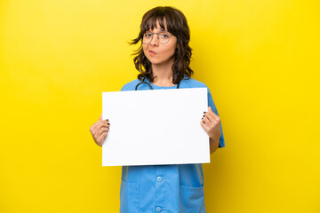 Young nurse doctor woman isolated on yellow background holding an empty placard