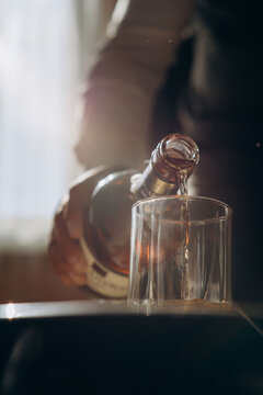 Man Pouring Whiskey Over Ice Cubes At Wooden Counter Bar, Drinking At Home Night Time. Drink After Work At Home. Man Drinking Whiskey After Work At Home.