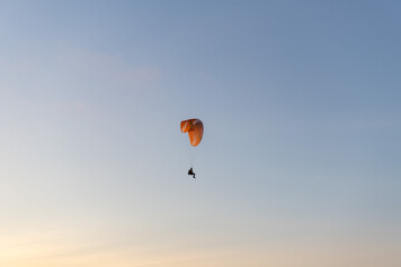 Paraglider flying over thesea shore at sunset. Paragliding sport concept.