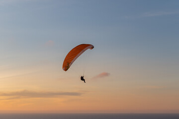 Paraglider flying over thesea shore at sunset. Paragliding sport concept.