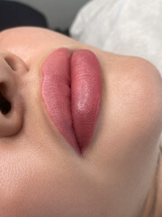 permanent makeup on the lips of a young woman of a delicate peach shade close-up - obrazy, fototapety, plakaty