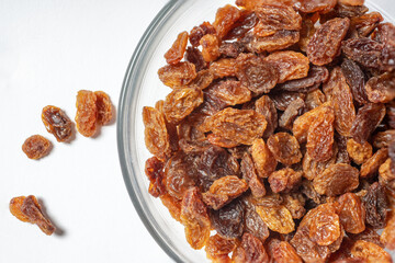 Close-up of a pile of seedless sultanas, made from green seedless grapes, are placed in a glass bowl on a white background. Dried fruit. Top view.