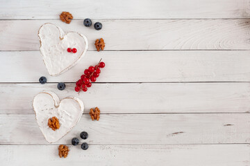 Fototapeta na wymiar Heart shape cheese with berries and walnuts on the wooden background