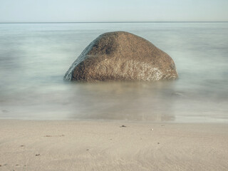 Round stone in the foreground on sandy beach. Baltic Sea at island