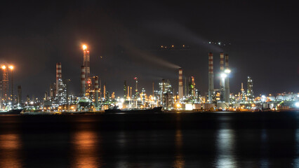 Fototapeta na wymiar Oil refinery plant at night. Long exposure of factory lights reflection on sea. Noise and grain included.