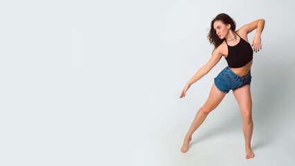 Fototapeta na wymiar beautiful dancing woman in short shorts and a black tank top on a white background in the studio, copy space