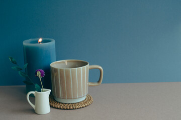 Cup and candle, dry flowers on table. navy blue wall background