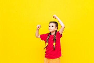 The little girl viciously shows her fists with her hands up. A disgruntled child is protesting against a yellow isolated background.