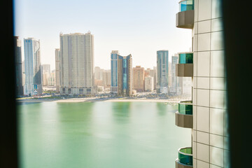 Panoramic window view to high buildings with balconies and marina in Sharjah district. Rented...