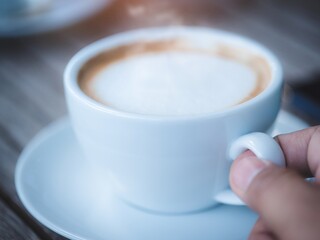 Man hand is holding a white coffee cup with smoking on wooden background
