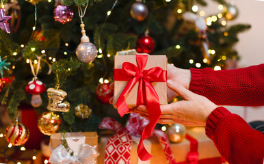 The girl gives a Christmas present, decorated with a red ribbon. Christmas photo with copy space, blurry lights, highlights, festive mood. concept of christmas holidays