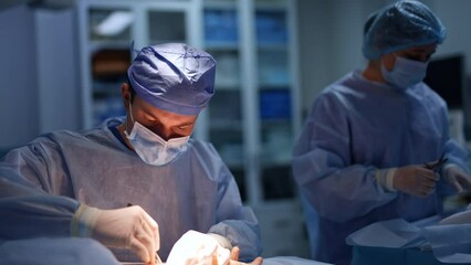 Attentive surgeon making a cut using the scalpel. Beginning of neurosurgical operation on arm. Female nurse preparing materials and tool at backdrop.