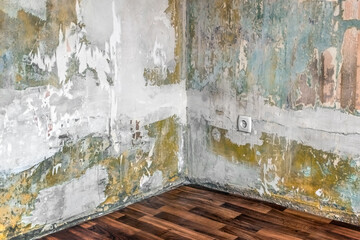 Corner in an empty room with old shabby walls with a European electrical outlet and no wallpaper....