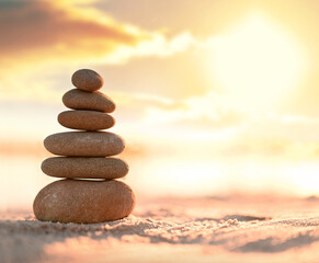Balanced pebble pyramid on the beach. Abstract warm sunset bokeh with sand on the background. Zen stones on the sea beach.