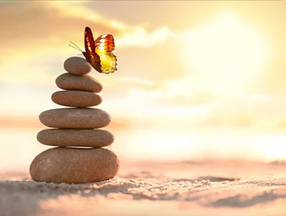 Fotobehang Zen Stenen Balanced pebble pyramid and butterfly on the beach. Abstract warm sunset bokeh with sand on the background. Zen stones on the sea beach.  © Belight