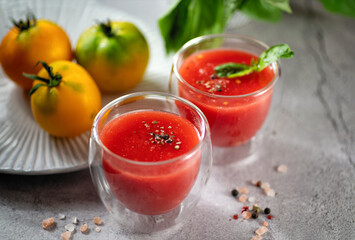 Freshly squeezed tomato juice with basil leaves, salt and pepper in glass glasses on a light gray background, horizontal format