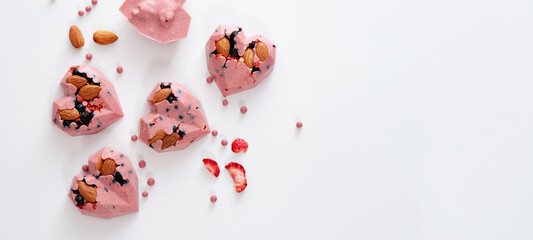 Heart-shaped candies with pink chocolate with strawberries, blueberries and almonds, handmade, top view, on white background, banner, place for text