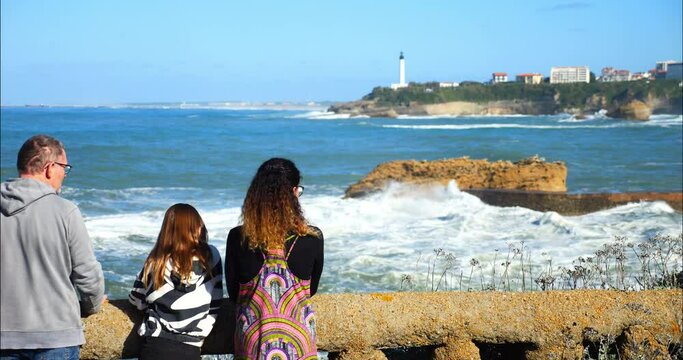 Mom and her daughter watching the swell breaking on the beach of Biarritz with its famous lighthouse on the horizon