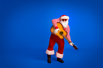 Full length photo of pensioner old man play guitar entertain party wear santa costume suspenders sunglass striped shirt headwear boots isolated red color background