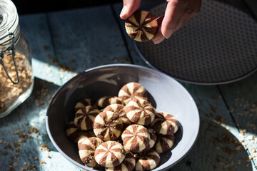 Sweet chocolate cookies on rustic wooden table with flakes. Woman hand holding cookies