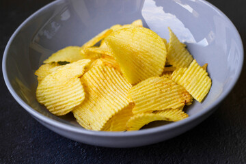 Crispy potato chips in blue bowl on a black slate background