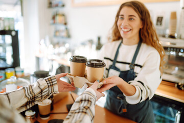 Smiling barista- girl giving take away coffee cups to a customers.  