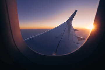 Romantic view from airplane window over wing during beautiful sunset. Sun is on horizon and colors...