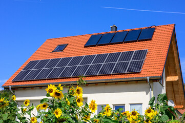 Modernes Solardach vor blauem Himmel mit Sonnenblumen im Vordergrund