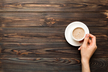 Minimalistic style woman hand holding a cup of coffee on Colored background. Flat lay, top view cappuccino cup. Empty place for text, copy space. Coffee addiction. Top view, flat lay