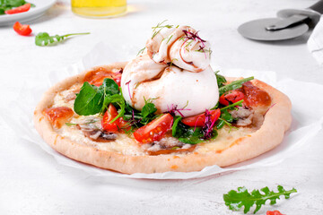Pizza with mushrooms served with burrata cheese, arugula and cherry tomato on parchment paper. Italian and Mediterranean cuisine