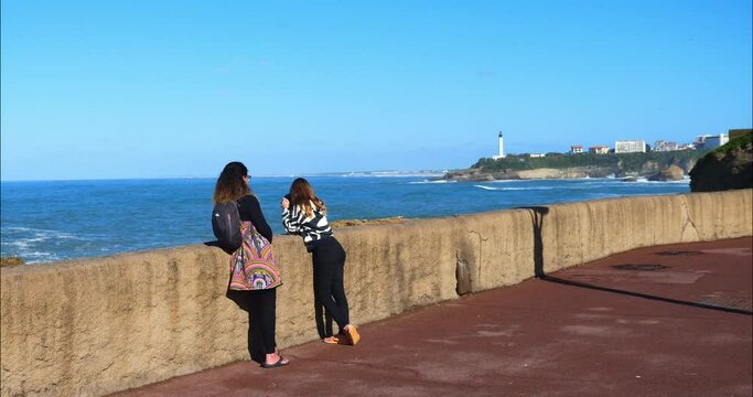Mum and her daughter taking photos of the swell breaking on the beach of Biarritz in the Basque Country