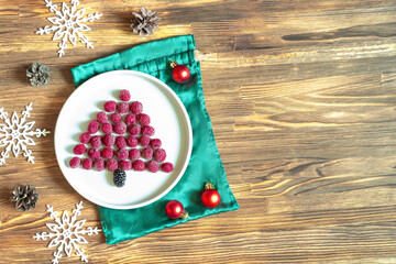 Funny Christmas tree shaped sweet fresh raspberry berry on plate on wooden background for kids...