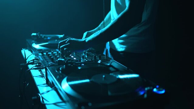 Dj mixing vinyl records on a techno party in dark nightclub. Professional club disc jockey mixing music set on a concert stage in blue lights