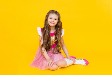 The little lady is sitting on a yellow isolated background. A beautiful girl with long hair in a...