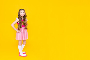 A beautiful little girl in full height in a pink dress on a yellow isolated background. Happy little princess with long curly hair.