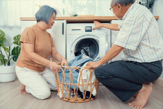 Senior couple working together to complete their household chores at the washing machine in a happy and contented manner. Husband and wife doing the usual tasks in the house.