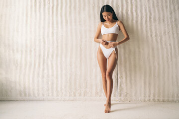 Asian slim woman measuring thin waist line with tape measure against textured wall with copy space