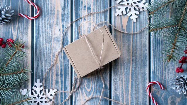 Stop motion video of Kraft cardboard gift box tied with rough jute rope on gray wooden background with branches of Christmas tree and Christmas decorations. Present opening, cut paper filler inside