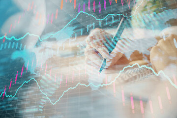 Financial forex graph displayed on hands taking notes background. Concept of research. Multi exposure