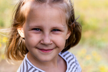 Smiling little girl in the park. Copy space. Happy child looking at the camera. Portrait of a laughing kid outside.