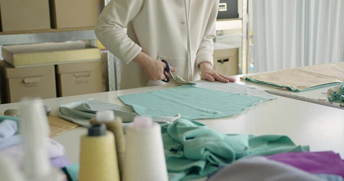 Woman cutting out a pattern paper in linen fabric. Fashion atelier concept