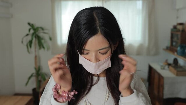 Asian young woman put a mask on reluctantly at home. Unhappy, Tired, Disappointed. Dolly in.