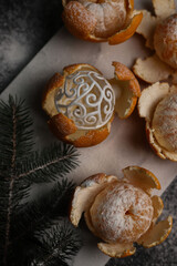 sweet orange juicy tangerines in a peeled peel lie on a black background and a black kitchen tray and in one peel a New Year's ball next to a spruce Christmas branch and sprinkled with white powder.fo