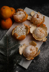 Naklejka na ściany i meble sweet orange juicy tangerines in a peeled peel lie on a black background and a black kitchen tray and in one peel a New Year's ball next to a spruce Christmas branch and sprinkled with white powder.fo